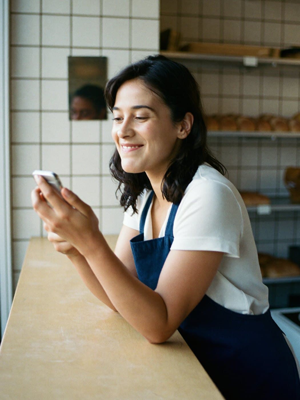 Dona de uma padaria confere um recebimento no celular, apoiada no balcão